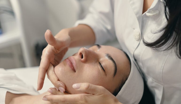 Beauty, spa and cosmetology concept. Young woman lies with closed eyes, cosmetologist making procedure for facial skin rejuvenation, facial massage.